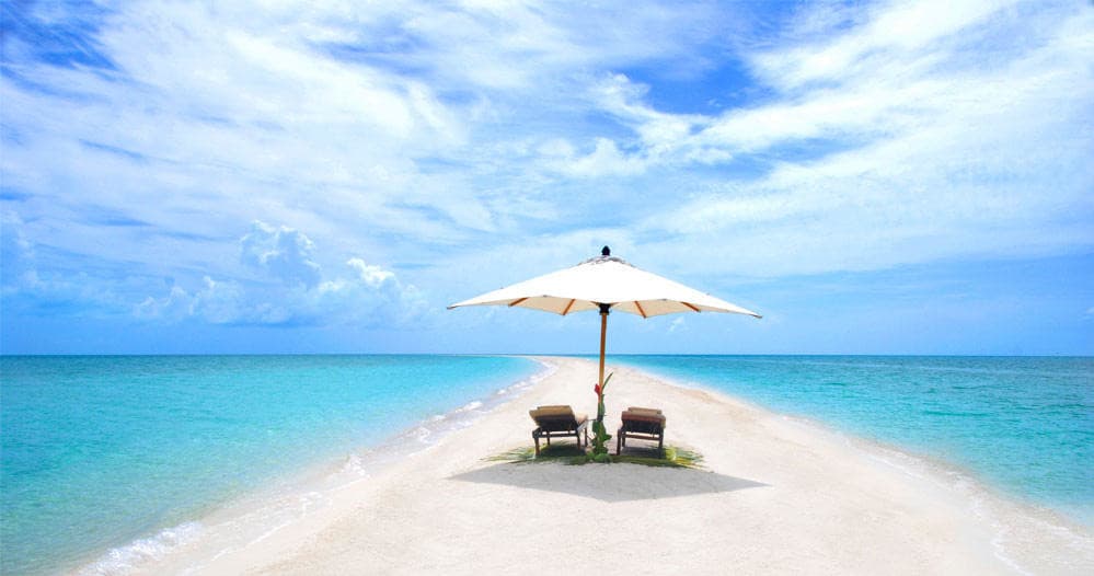 Beach umbrella and lounge chairs on tropical sandbar, clear sea