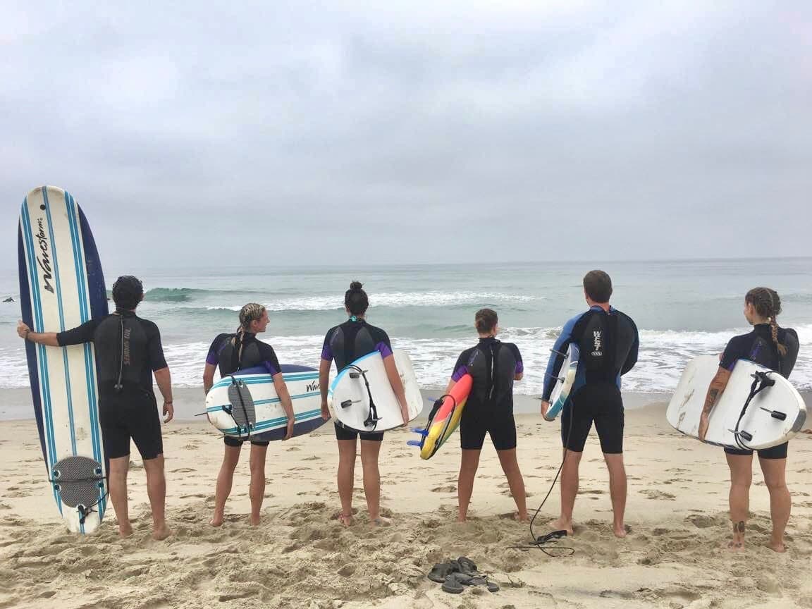 Group of surfers standing on sandy beach preparing to surf