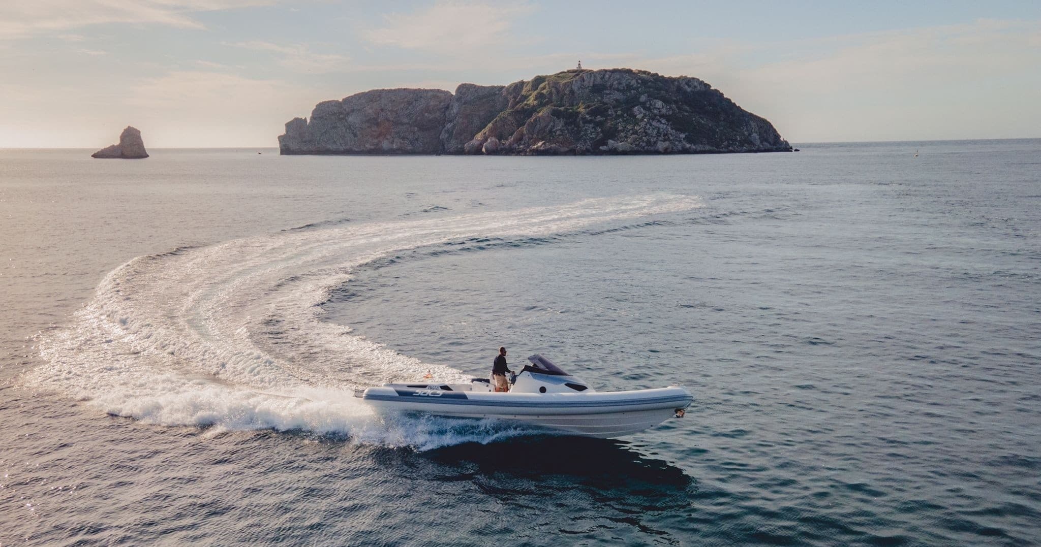 Speedboat cruising near rocky island, creating dynamic coastal wake