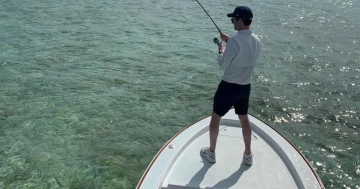 Angler fishing from bow of boat over clear shallow saltwater flats, sunny day