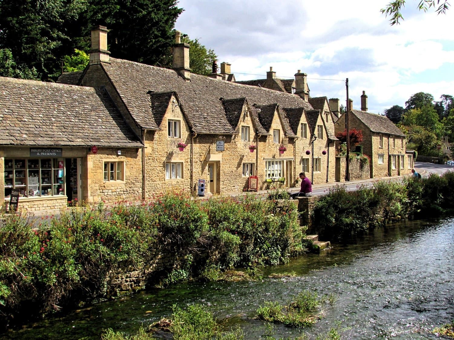 Cotswolds stone cottages along river in English countryside village