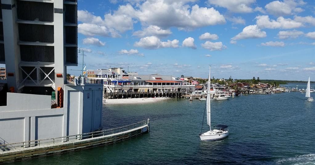Sailboat cruising past seaside marina and waterfront buildings