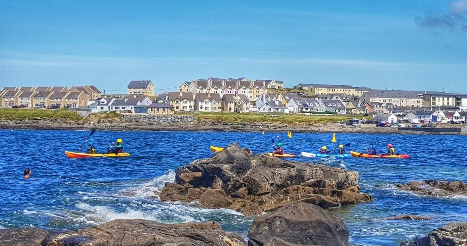 Sea kayakers paddling along rocky Atlantic coast near town