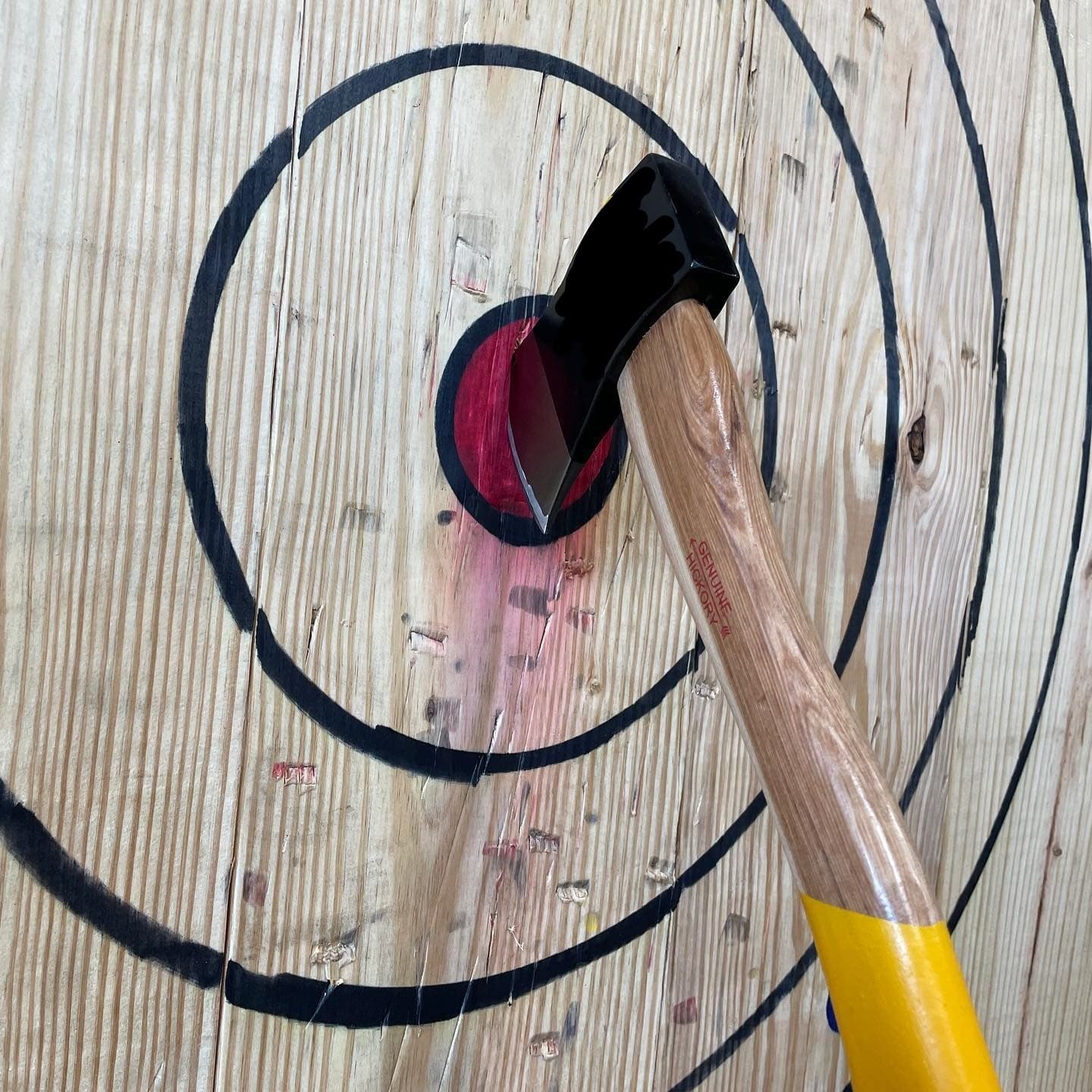 Axe with yellow-handled haft lodged in bullseye on wood target