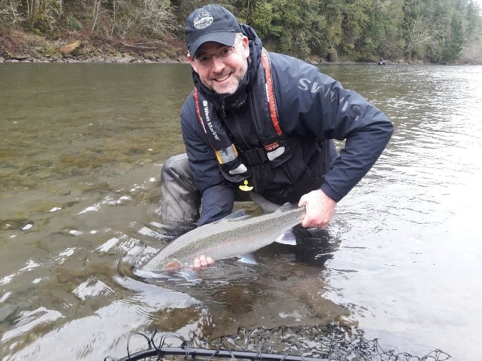 Angler releasing a wild salmon in a shallow river with bankside trees