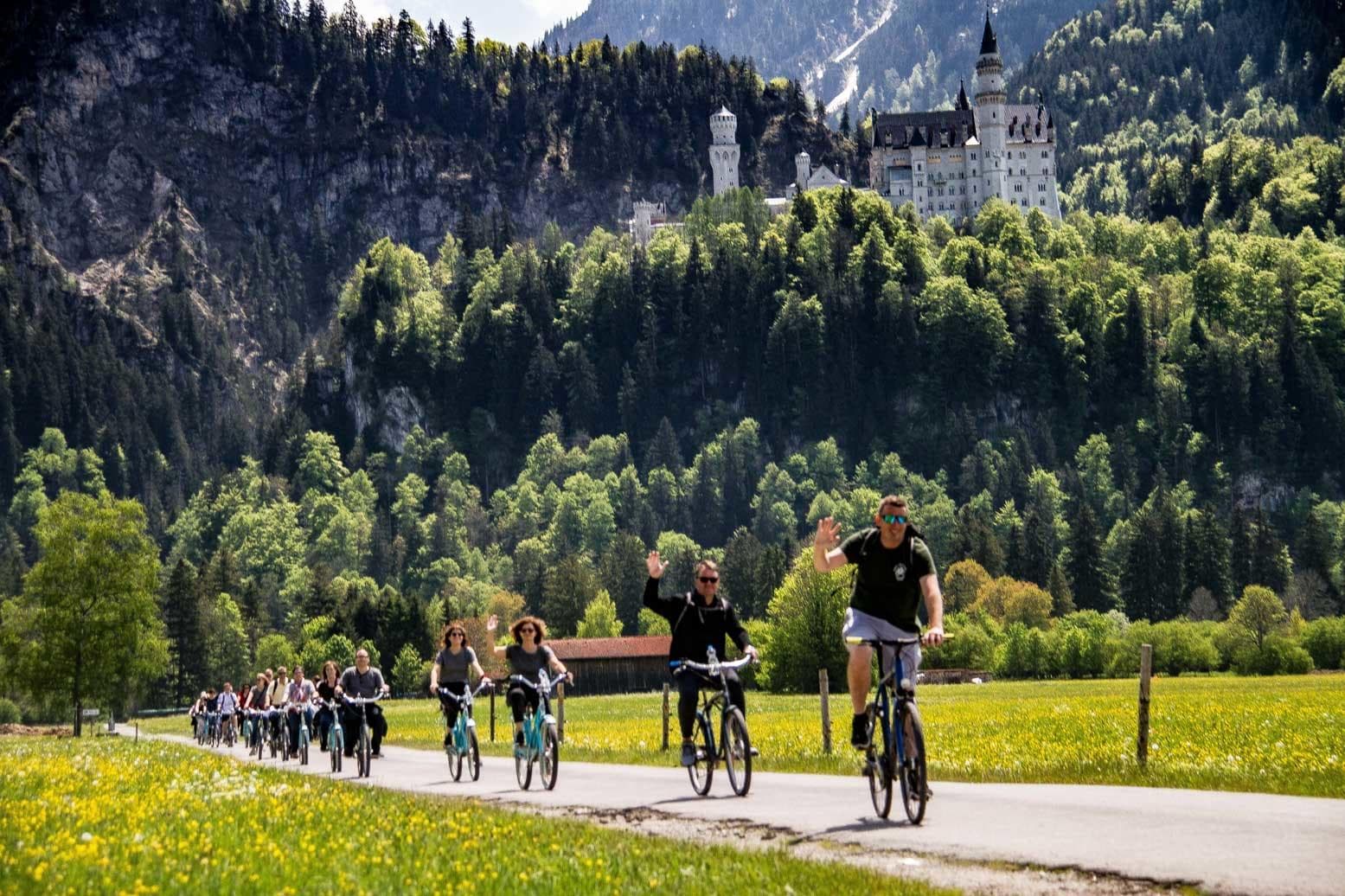 Cyclists riding toward Neuschwanstein-like castle in alpine valley