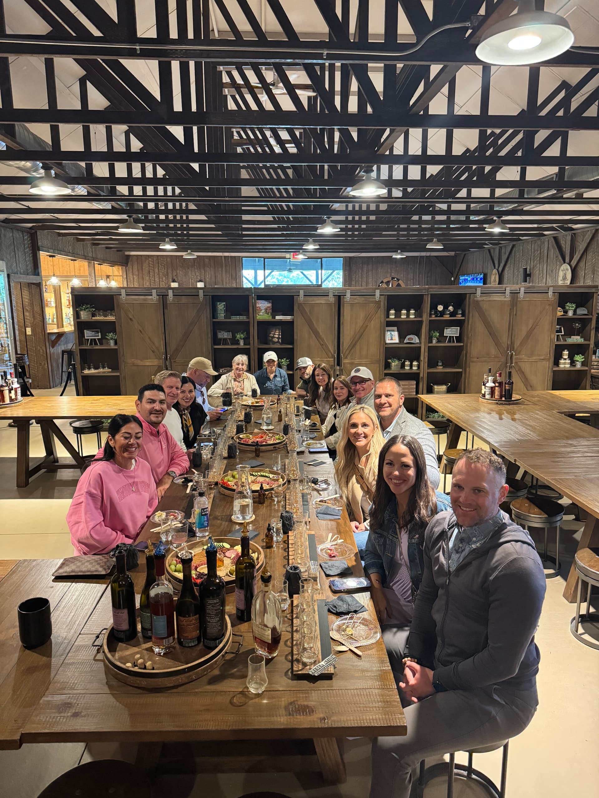 Large group bourbon tasting at rustic distillery table indoors