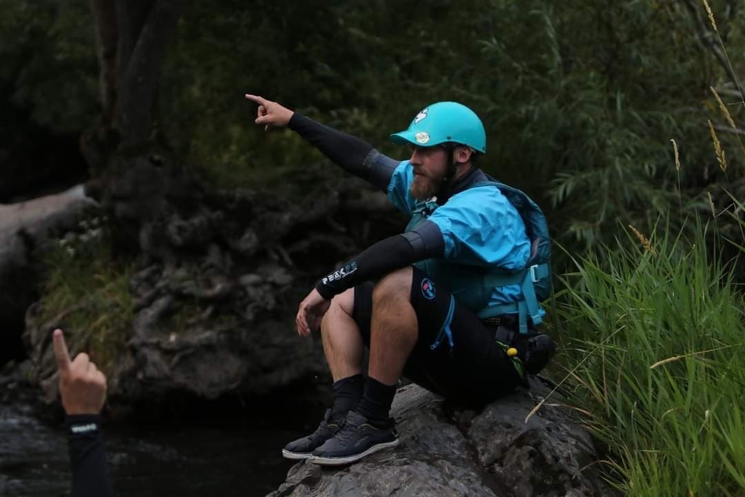 River guide pointing from rocky bank beside flowing stream