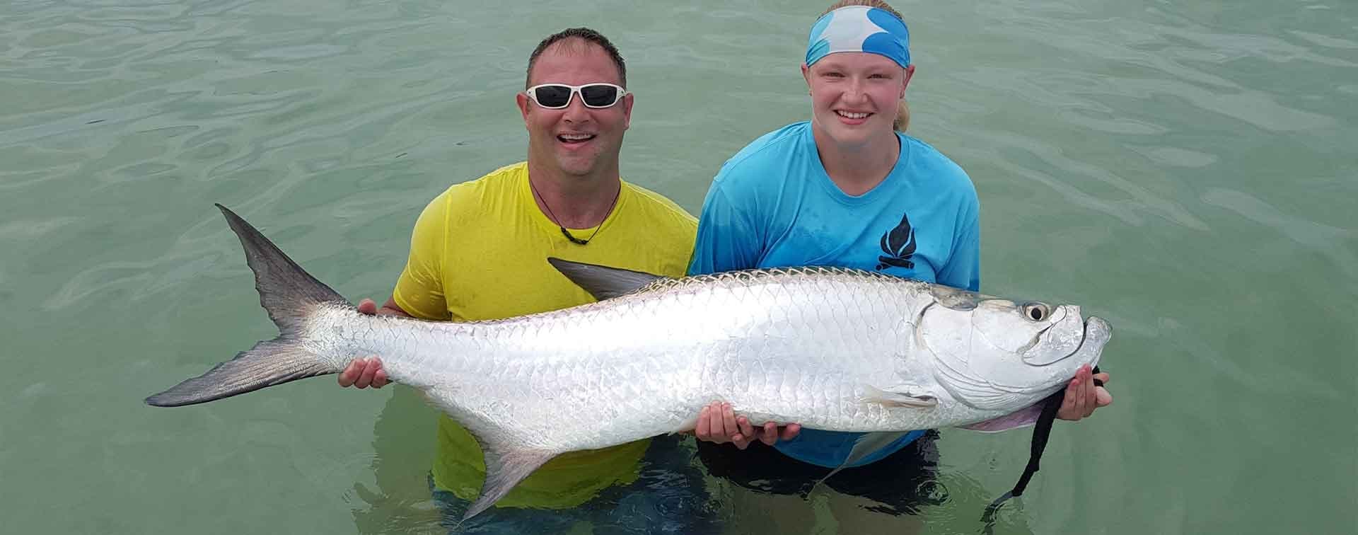 Two anglers holding large tarpon in shallow coastal waters