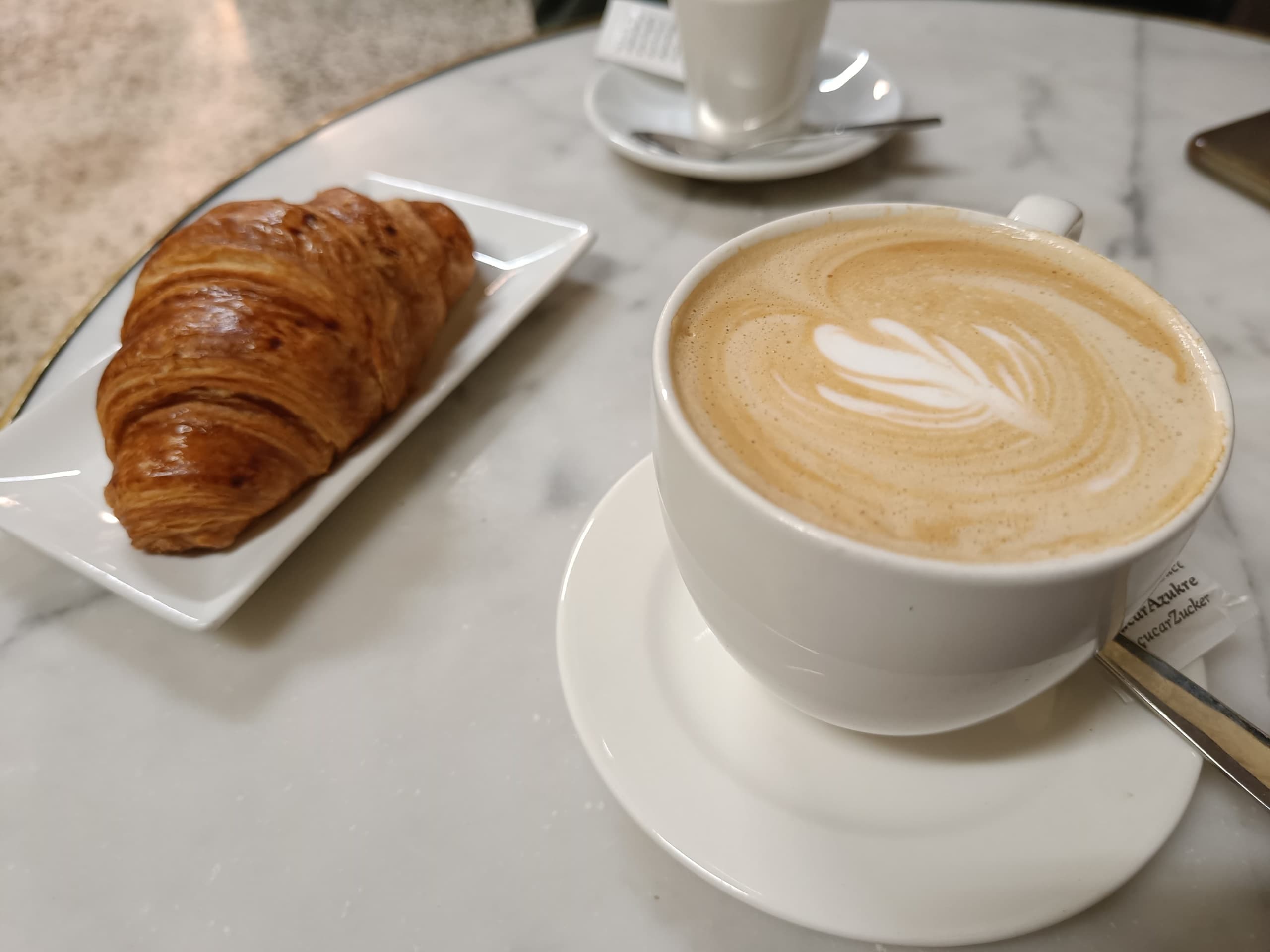 Cappuccino and croissant on marble café table for morning breakfast