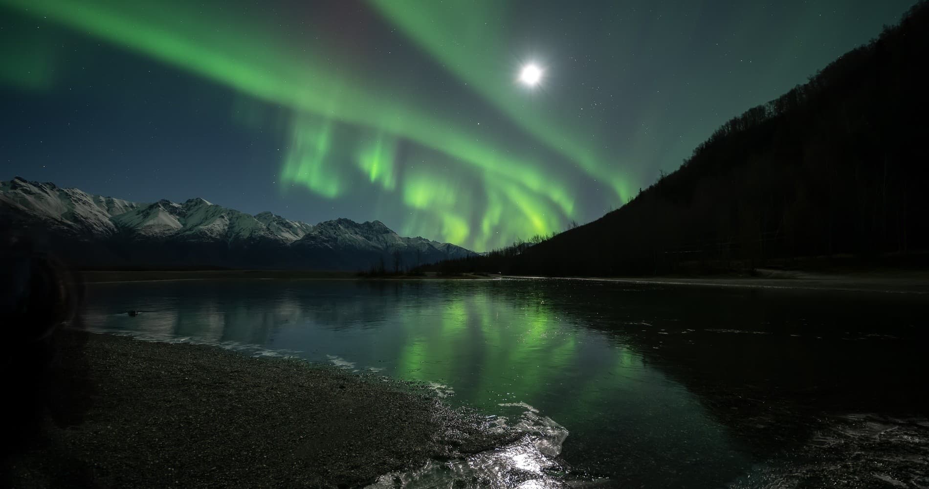 Northern lights reflected on still lake beneath mountain silhouettes