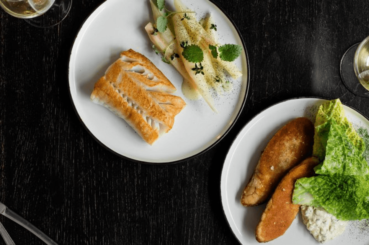 Plated Nordic seafood and sides served on dark tabletop at dining tour