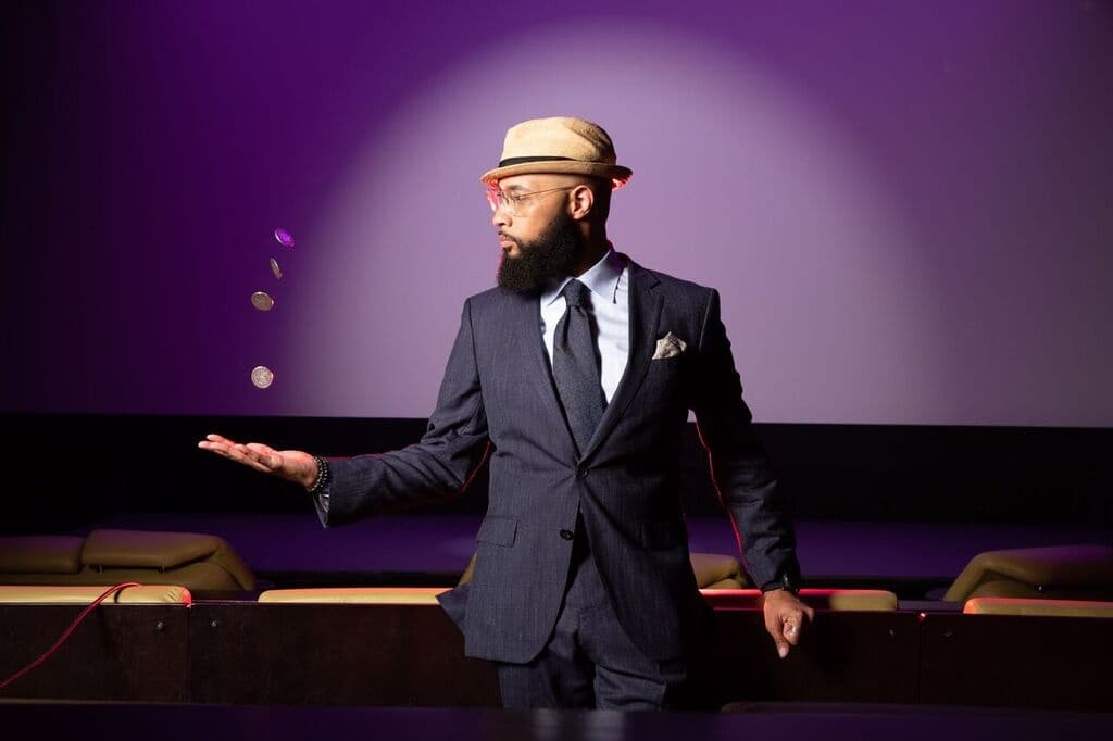 Magician performing on theater stage in suit and hat