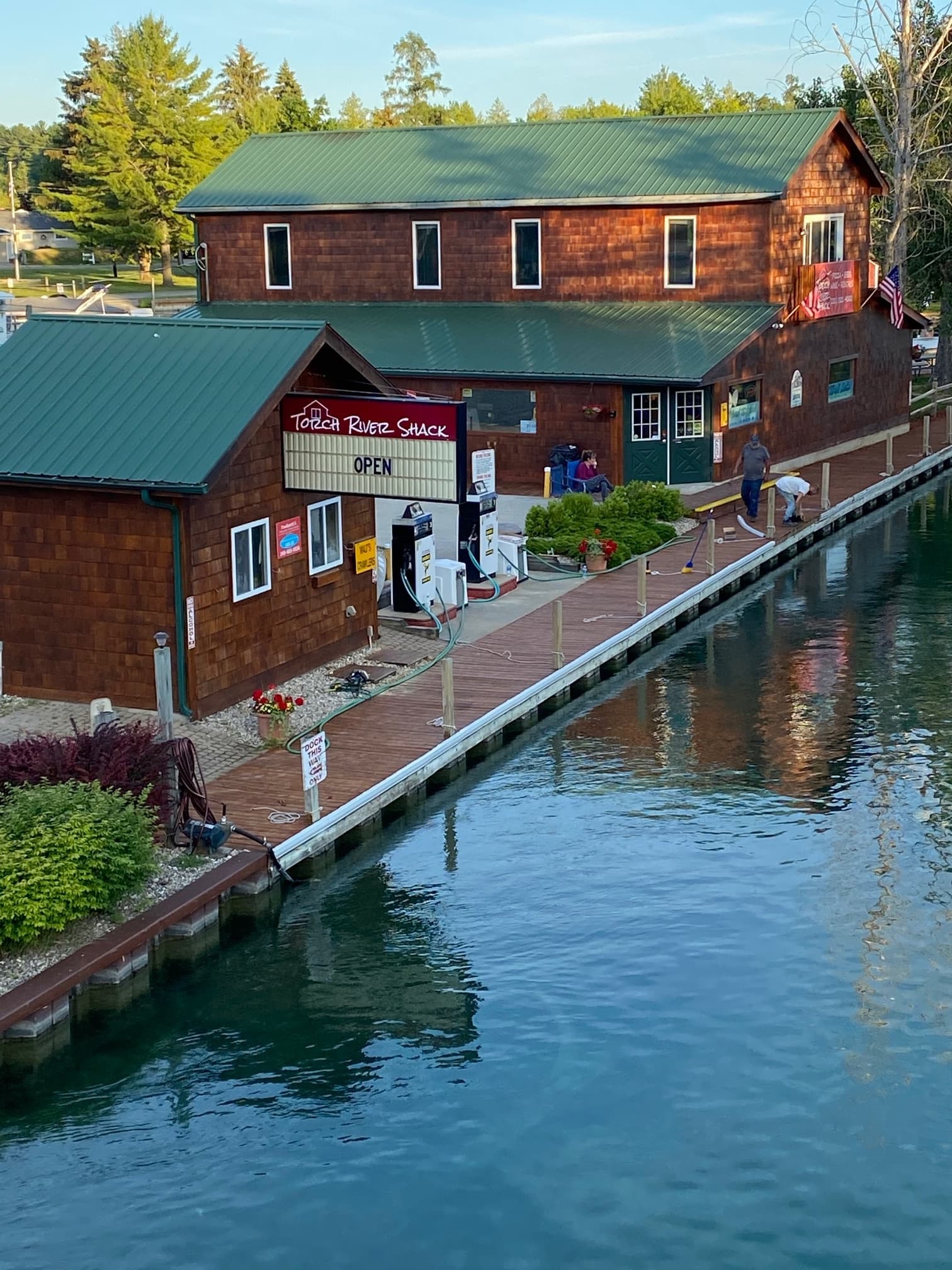 Riverside shack and dock beside calm canal with summer foliage