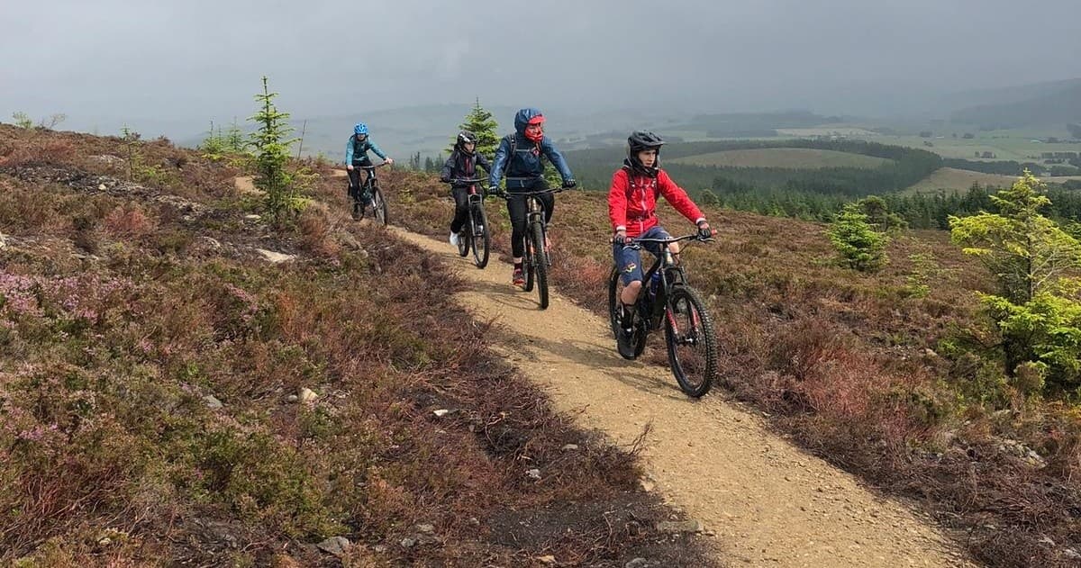 Group mountain biking along heather moor trail with vista