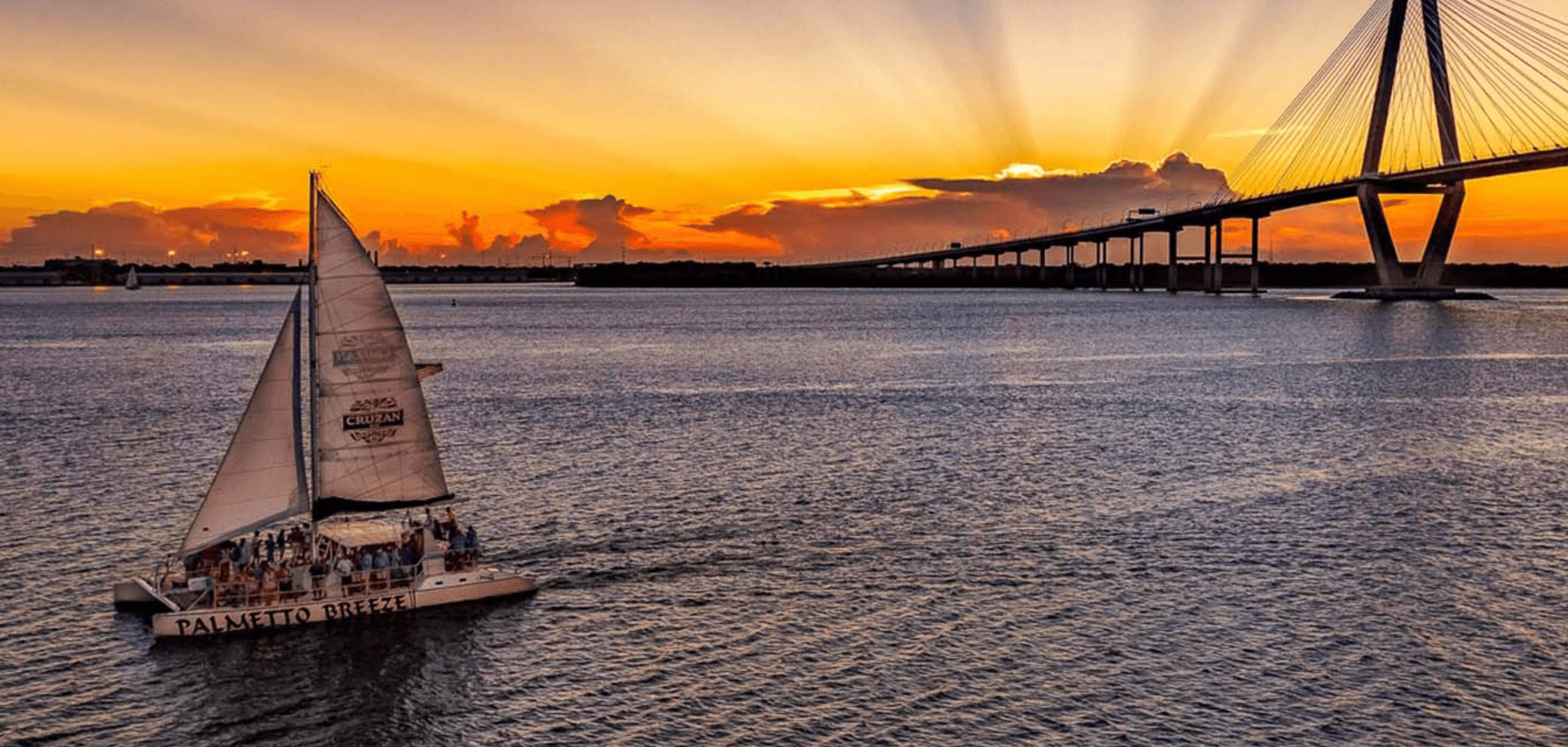 Sunset sailboat cruising near suspension bridge over harbor