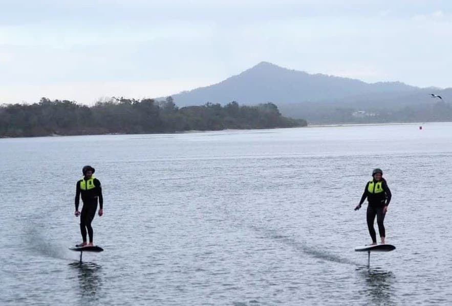 Two foilers cruising calm coastal water with mountain backdrop