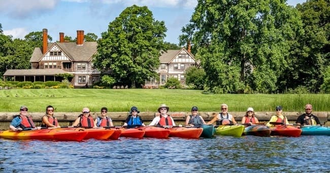 Group kayaking along scenic riverfront with historic estate backdrop