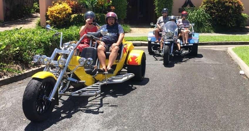 Two-person trike tour on sunny suburban road, riders smiling