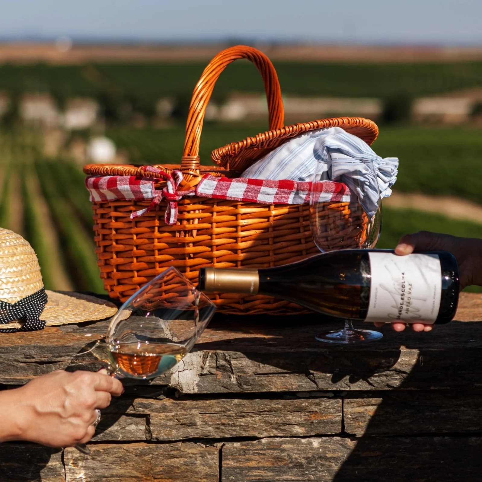 Picnic basket and wine being poured at vineyard picnic setting