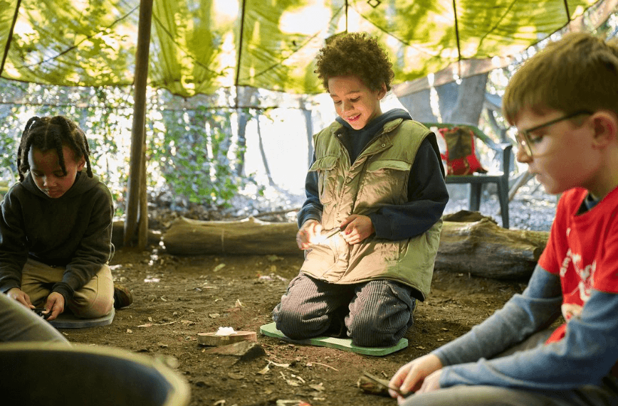 Children learning bushcraft around woodland campfire shelter
