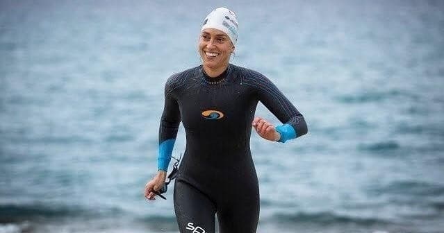 Open-water swimmer in wetsuit emerging from ocean during training