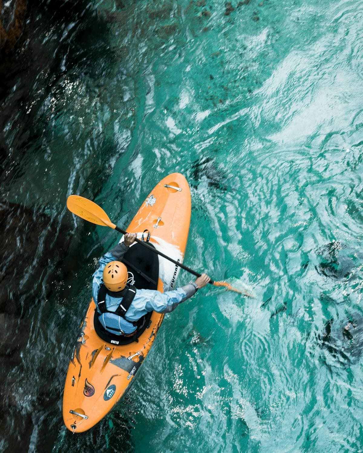 Aerial view orange kayak paddling through turquoise river rapids