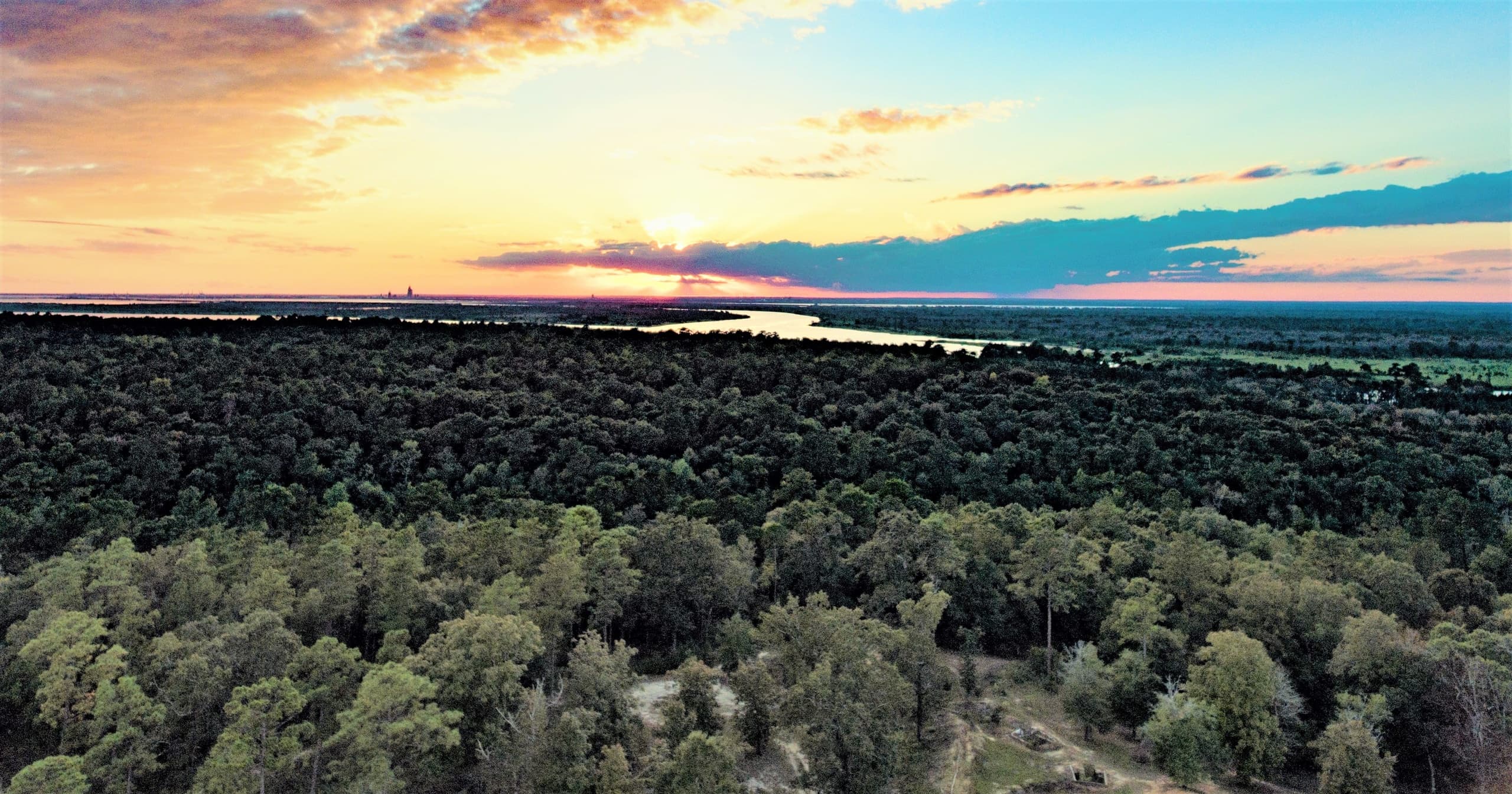 Aerial sunset over rolling forested hills and river valley