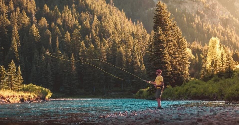 Fly fisherman casting in sunlit mountain river valley