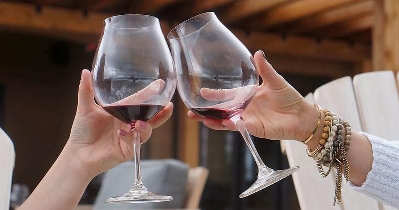 Close-up of two people clinking red wine glasses on patio