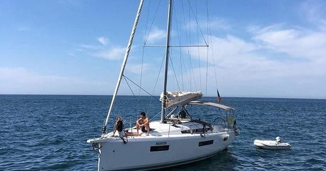 Sailboat anchored on open sea with crew enjoying ocean