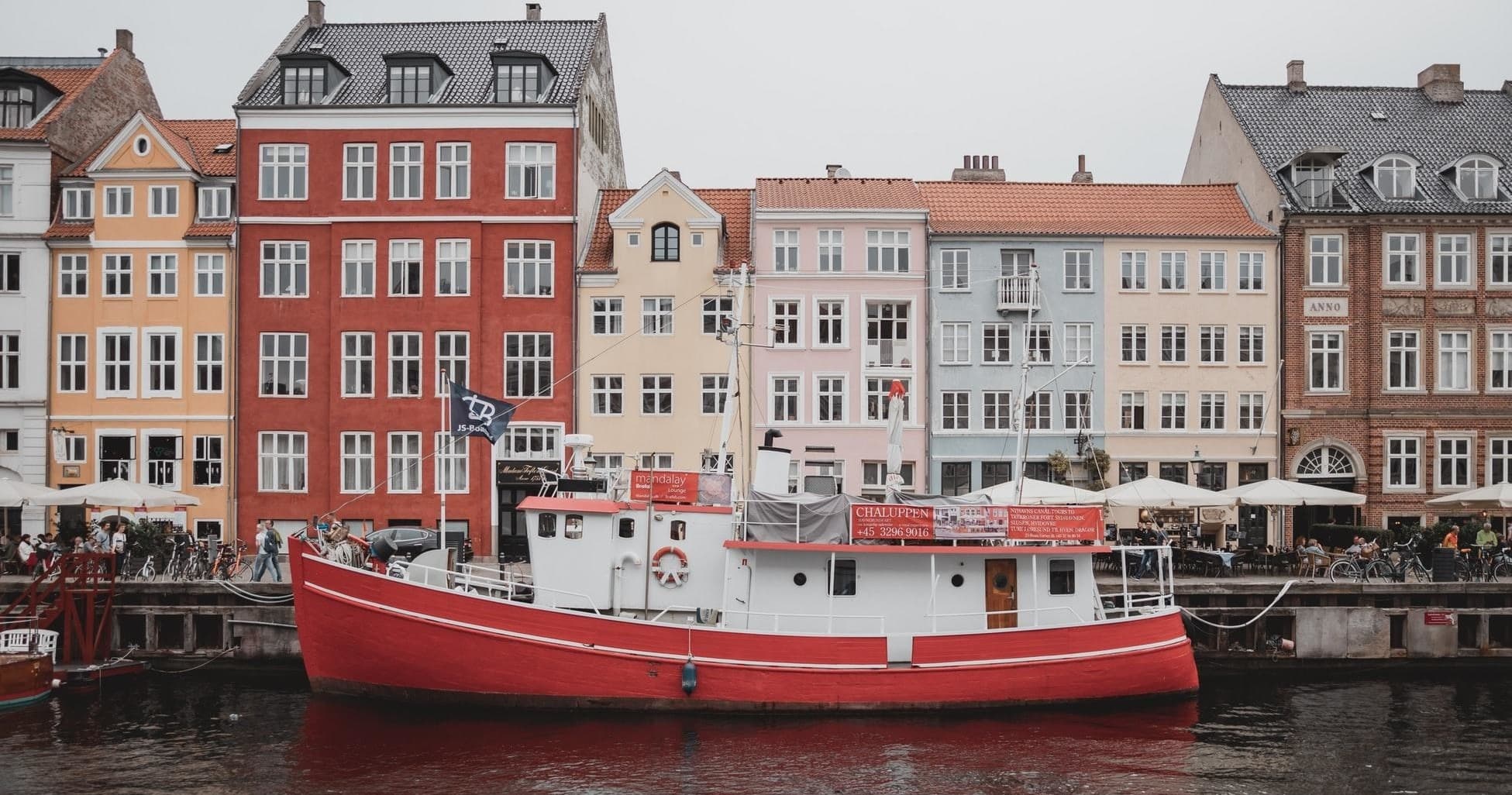 Red fishing boat docked by colorful Copenhagen harbor buildings