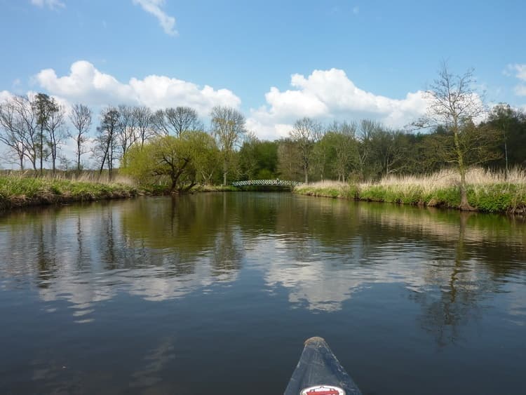 Kayak bow on calm river with open sky and distant trees