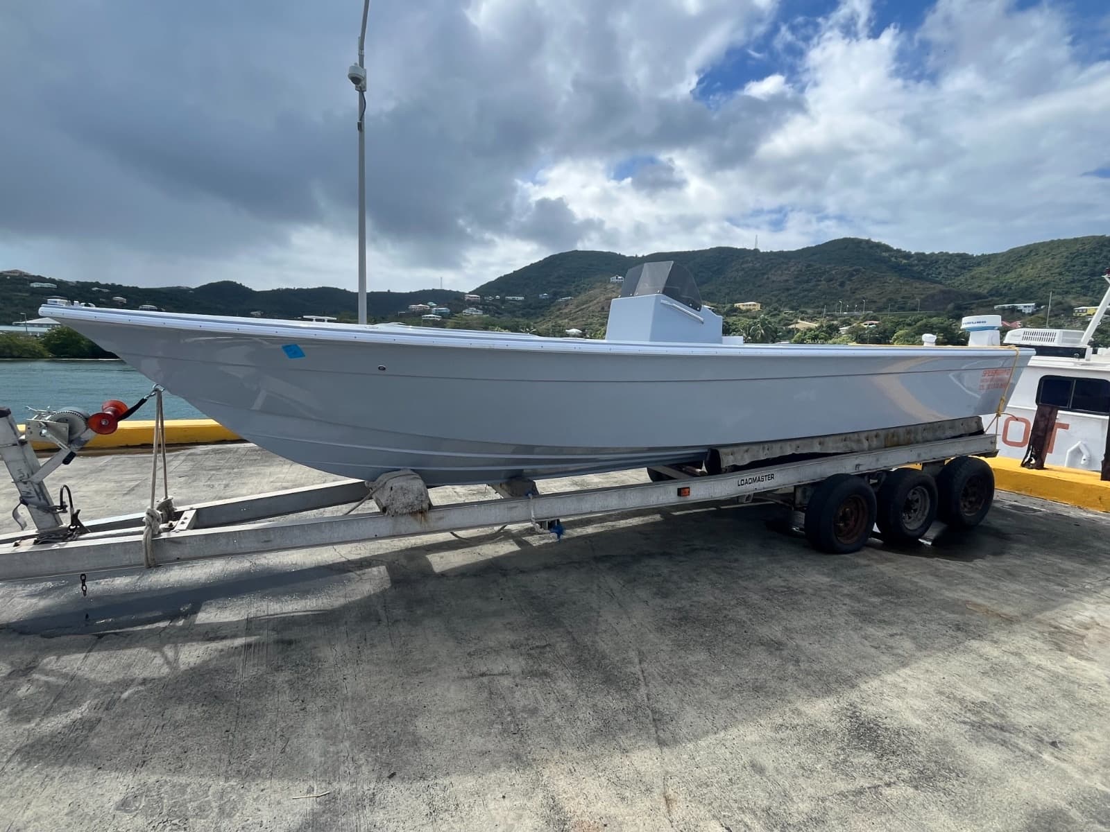 Center-console fishing boat on trailer at marina with coastal hills