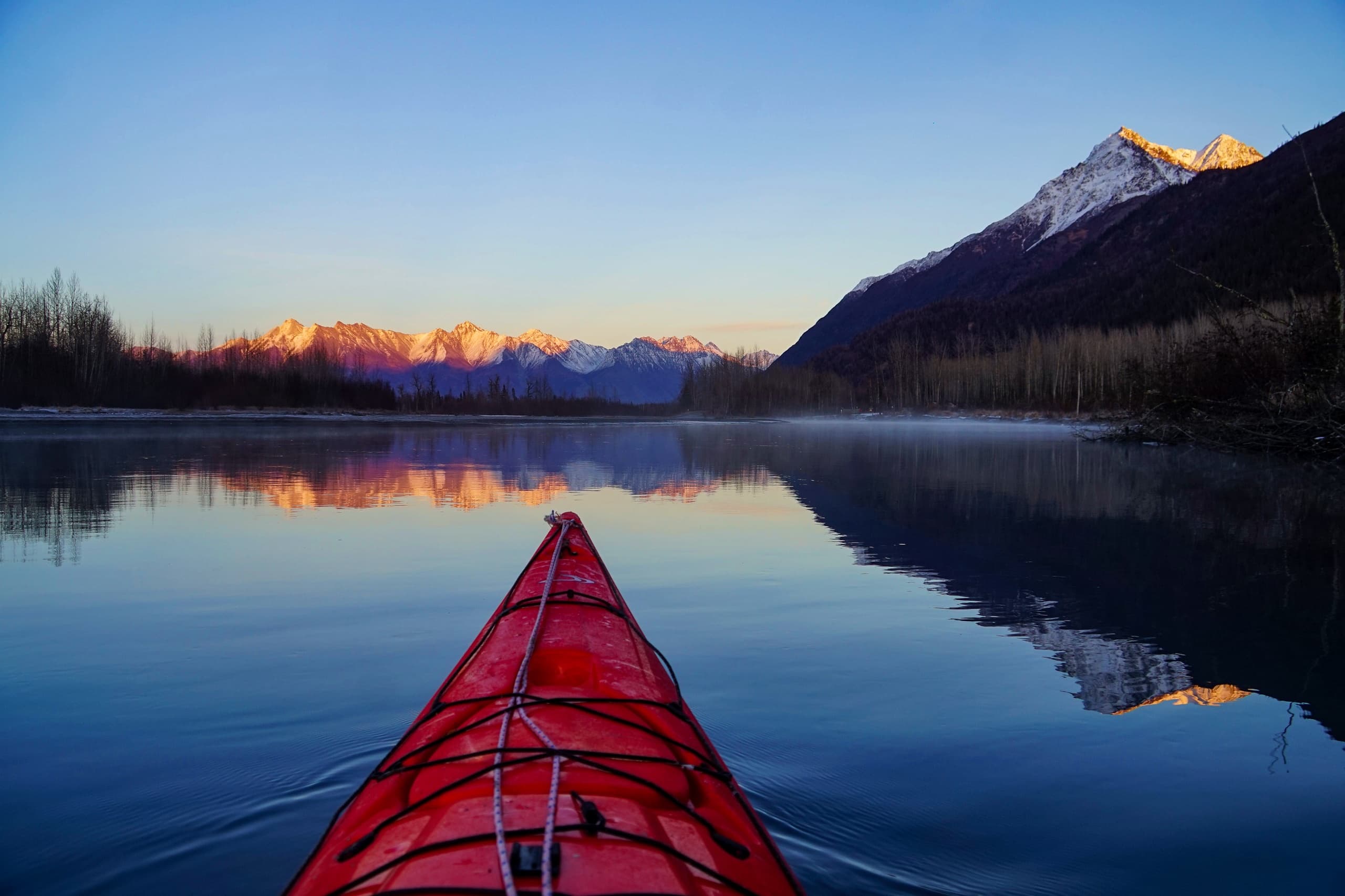 Red kayak bow gliding on calm reflective lake at sunrise