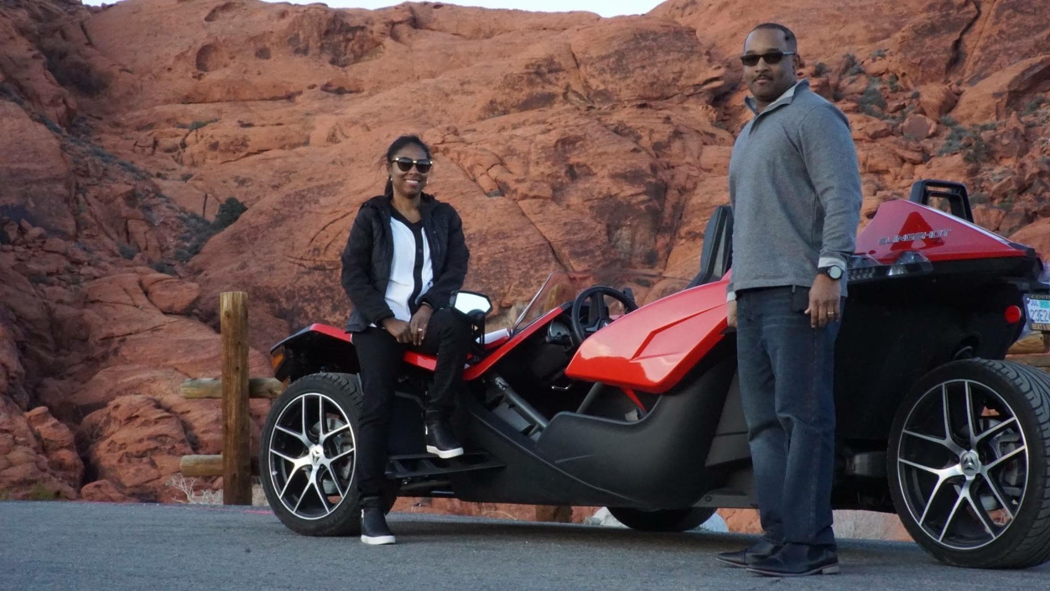 Couple with Polaris Slingshot by red-rock desert cliffs