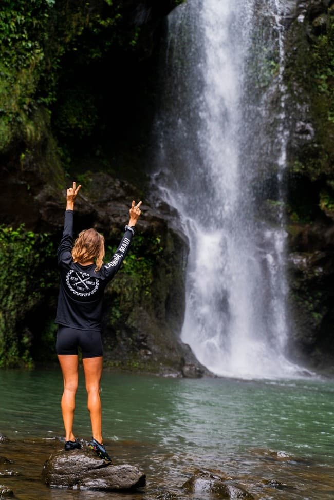 Person celebrating at tall waterfall in lush tropical Hawaiian cascade
