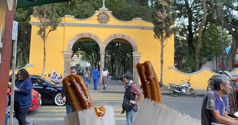 Street food churros in foreground by yellow archway outdoors