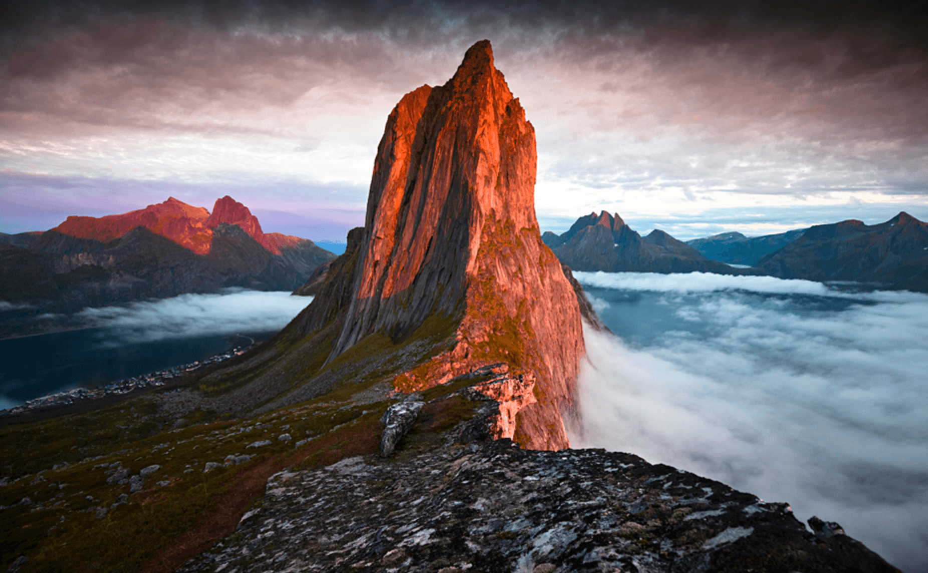 Jagged coastal mountain peak above fjord at golden hour, hiking