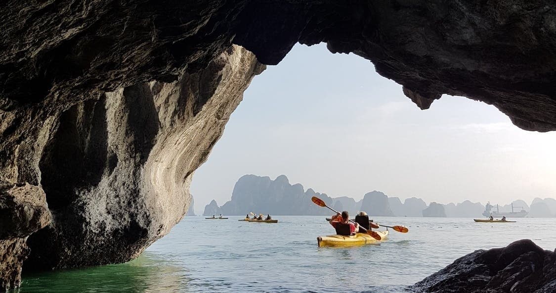 Kayakers paddling through sea cave toward limestone islands