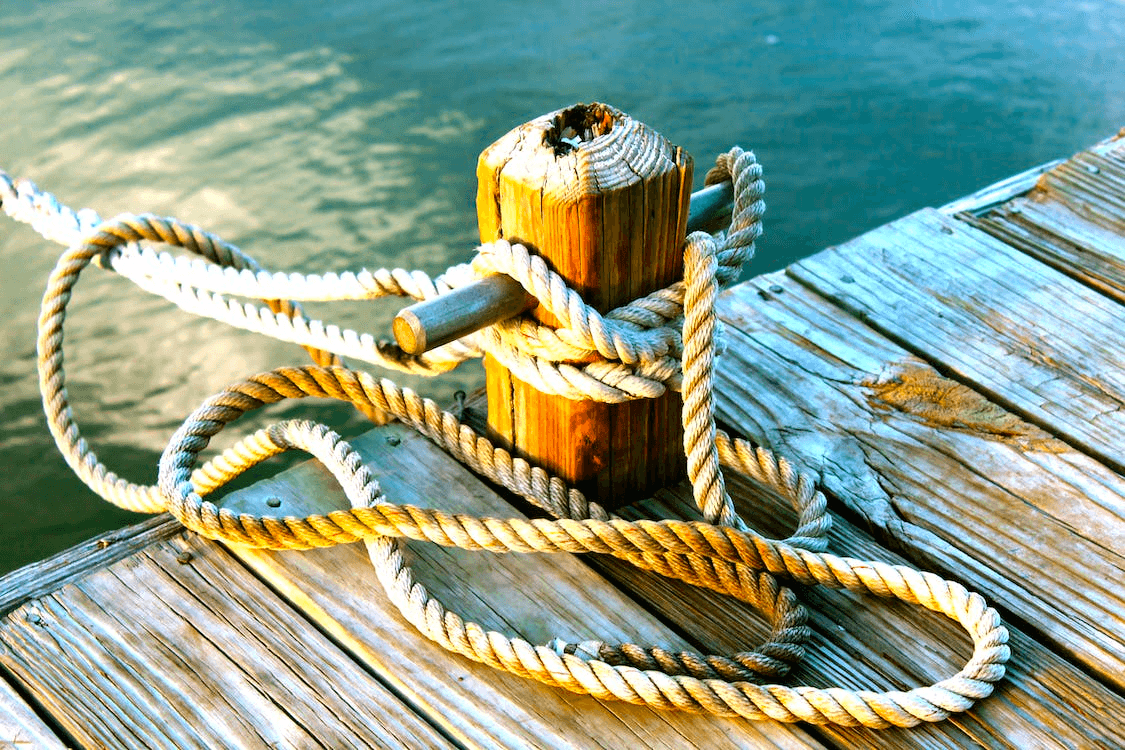 Rope secured to cleat on sunlit marina dock by calm water