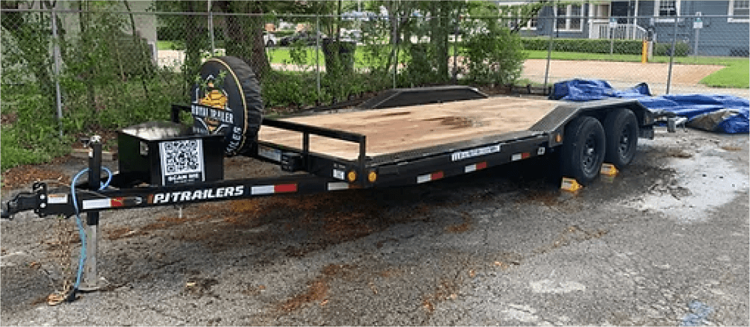 Dual-axle equipment trailer on gravel lot near greenery
