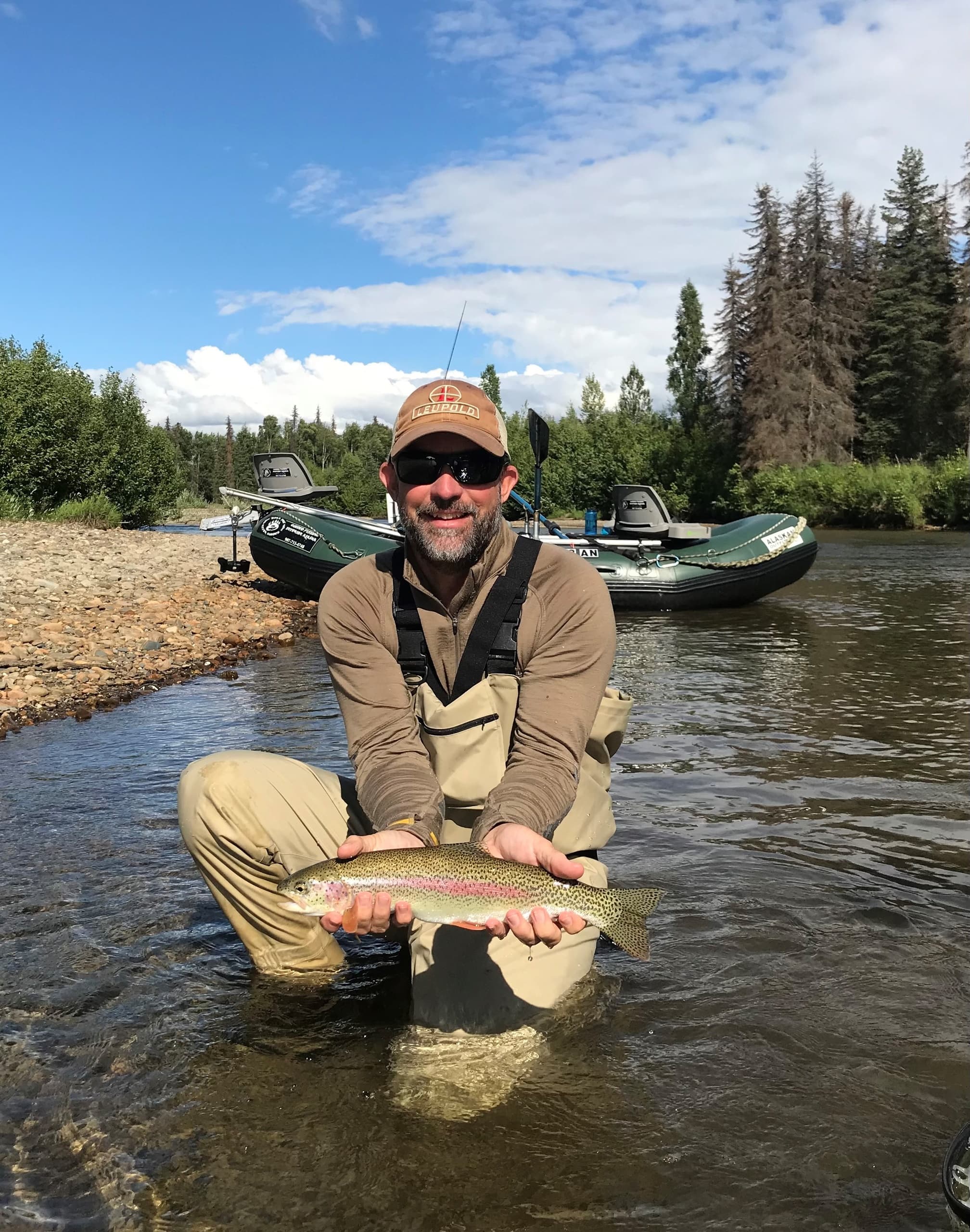 Angler kneeling in river holding rainbow trout in Alaska