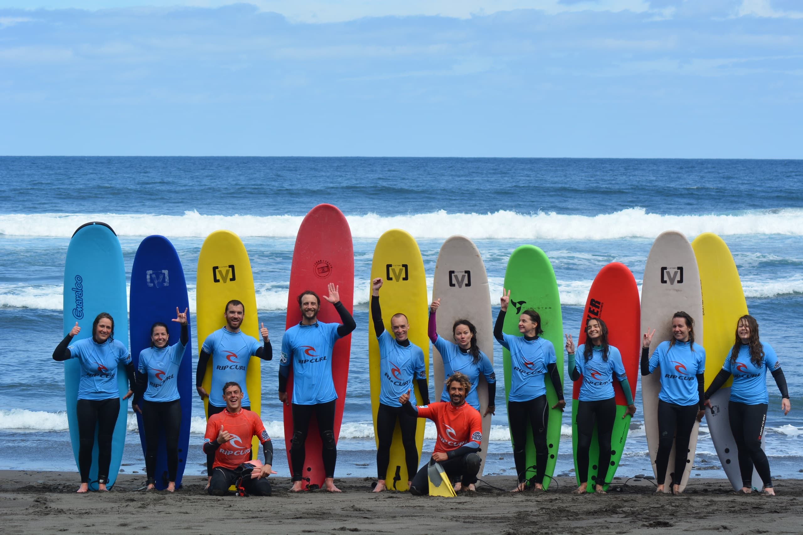 Group of surfers posing with colorful boards on sandy beach