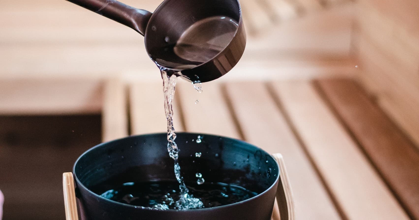 Sauna ladle pouring water over hot stones in wooden sauna