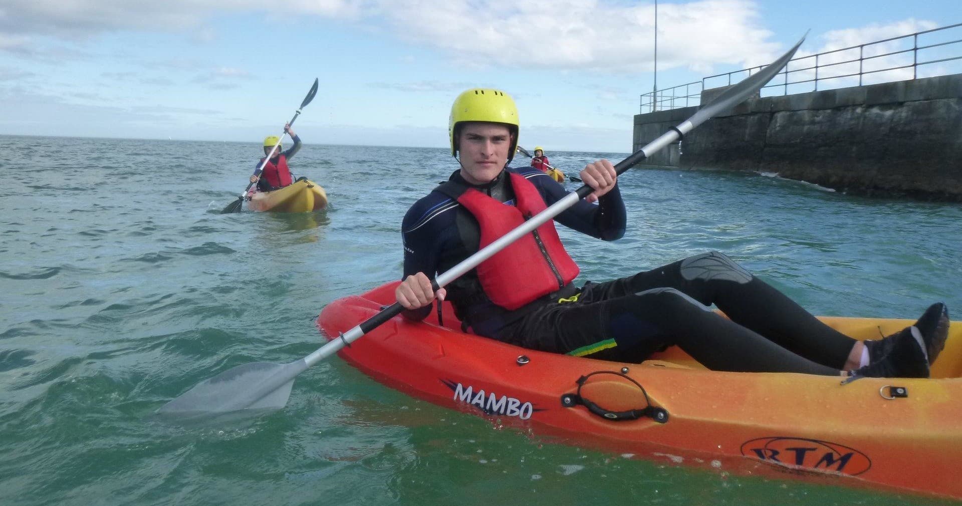 Close-up kayaker paddling offshore with harbor wall background
