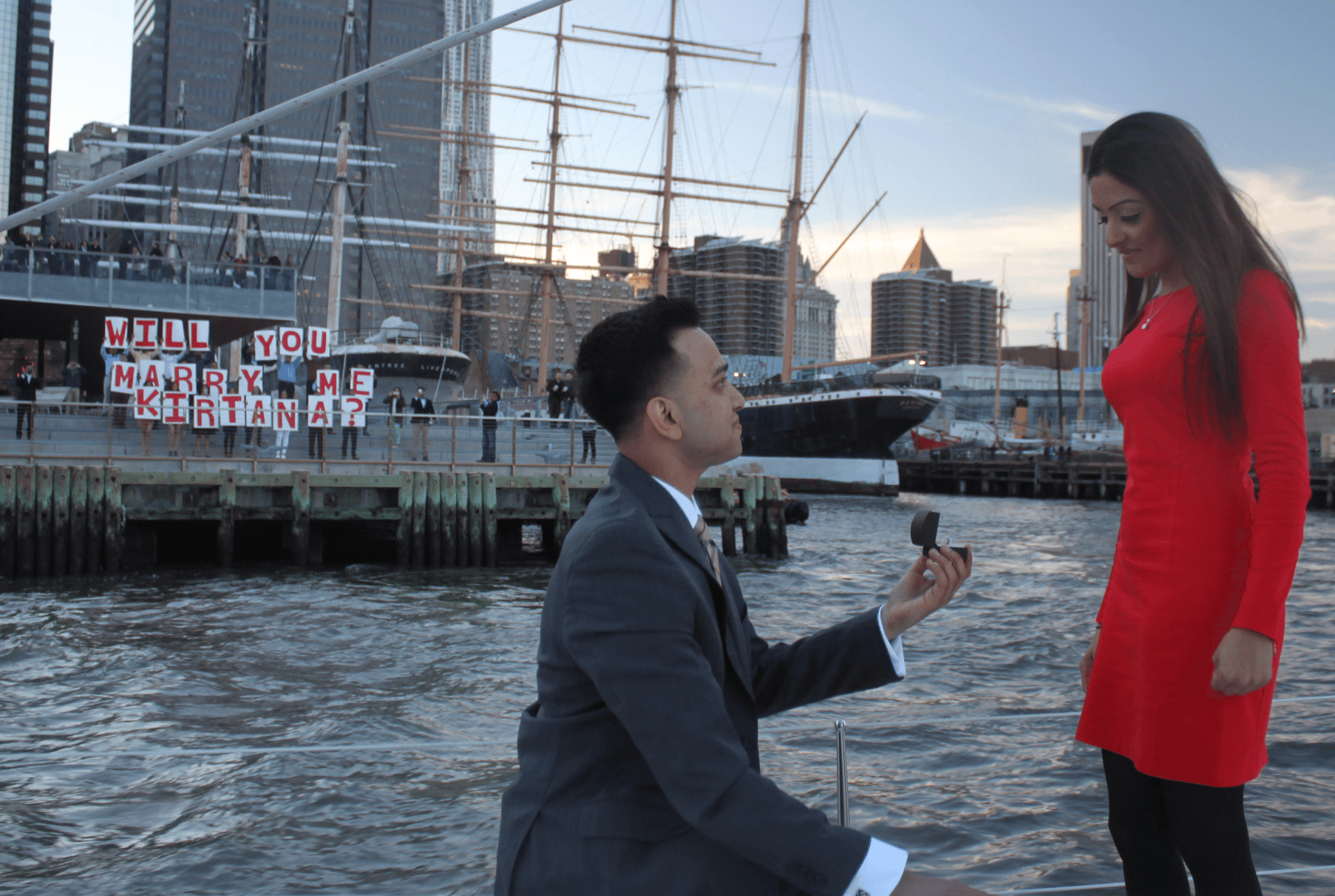 Couple engagement proposal on waterfront pier with city skyline backdrop