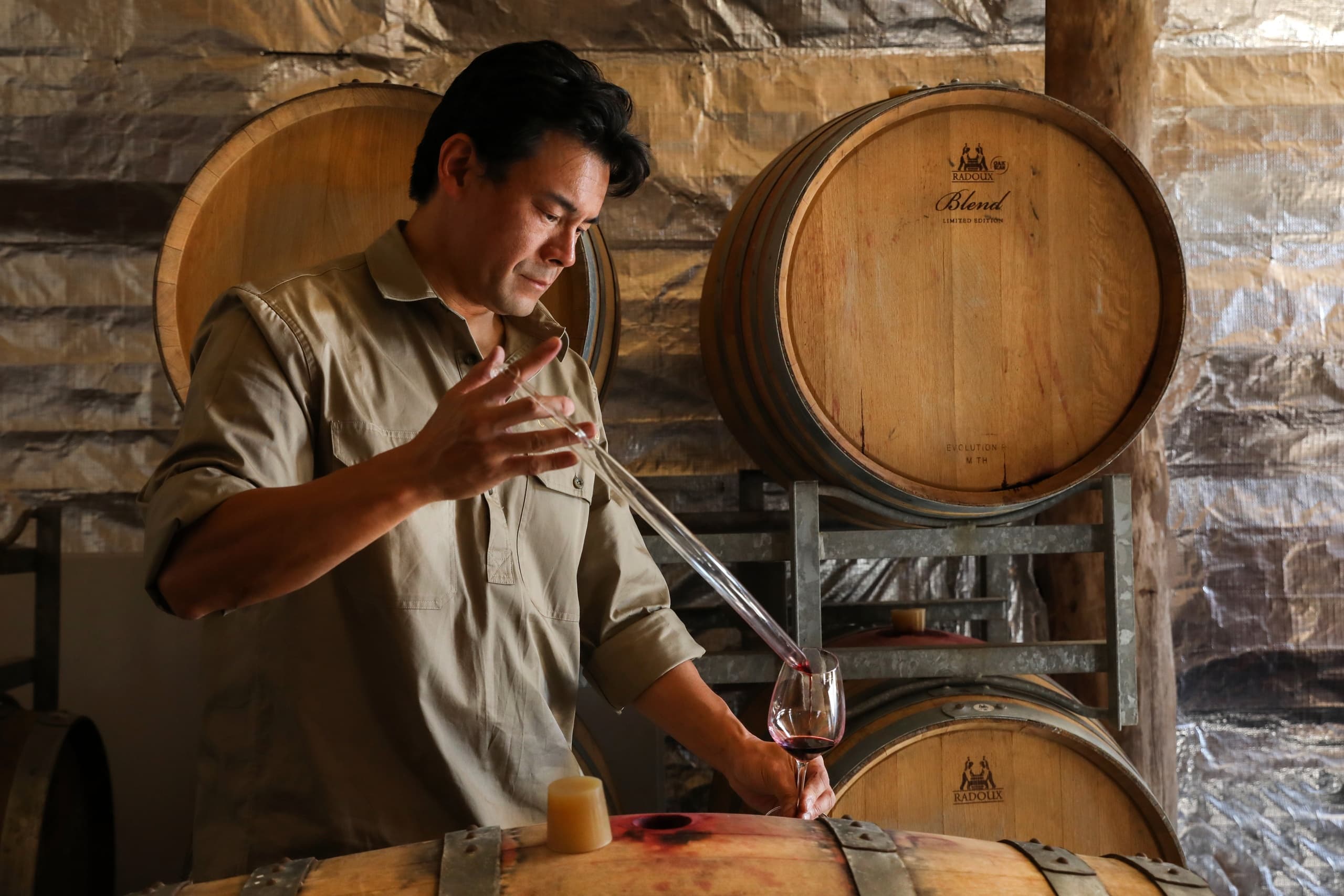 Winemaker sampling wine from barrel in rustic cellar room