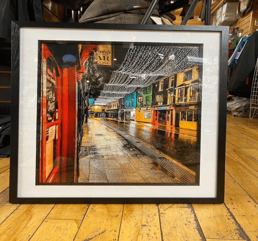 Framed rainy street photograph displayed on wooden floor inside gallery shop