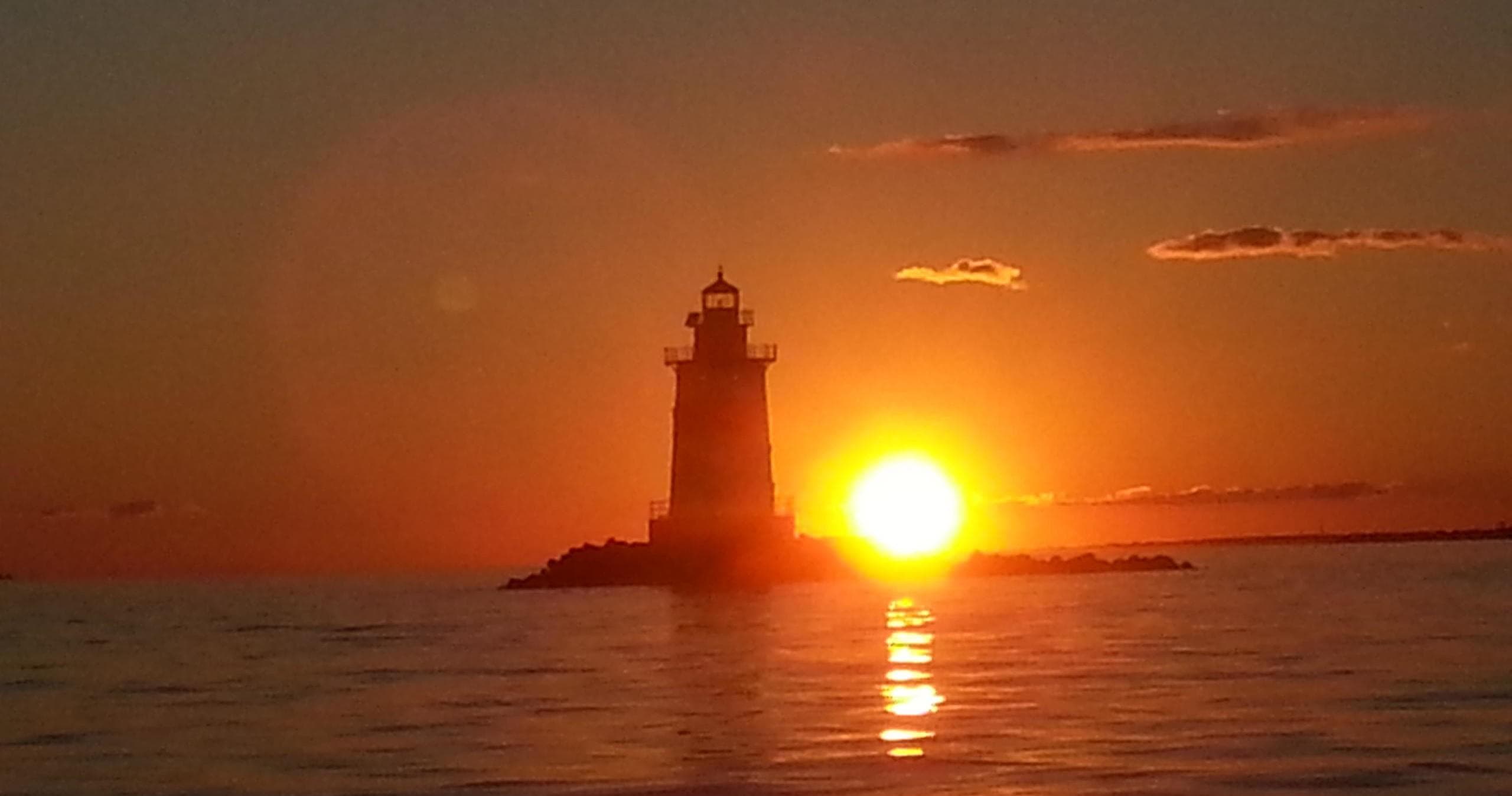 Lighthouse silhouetted at sunset over calm ocean, dramatic coastal view